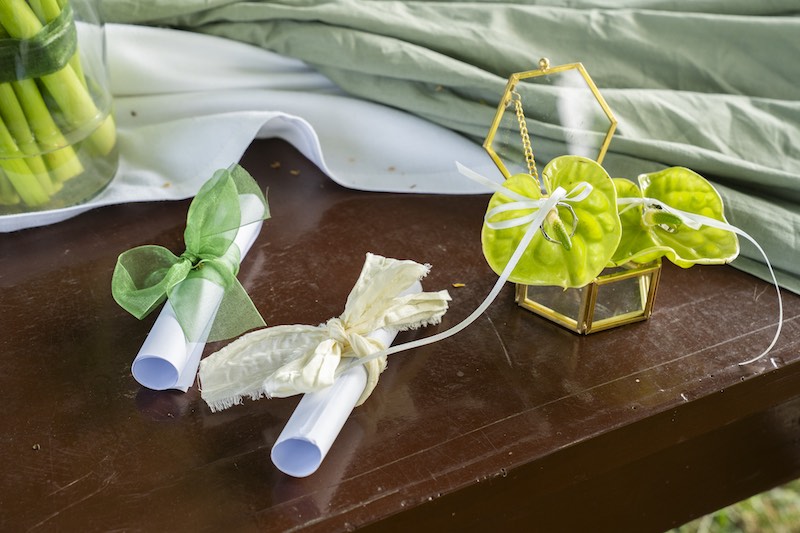 In questa foto, il dettaglio dell'allestimento del luogo della cerimonia realizzato da OttoQuattro Eventi con le promesse dei due sposi e il portafedi decorato con anthurium di colore verde