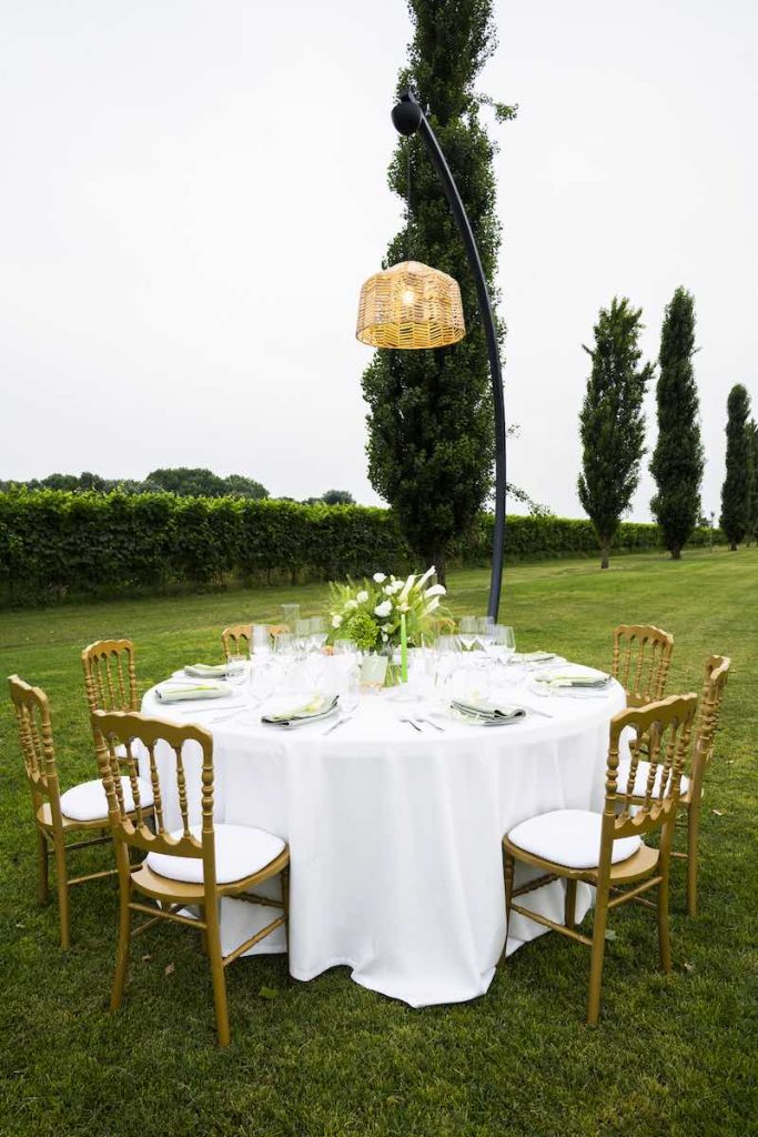 In questa foto un tavolo per un ricevimento di nozze di forma rotonda con tovagliato di colore bianco sormontato da un lampadario in vimini