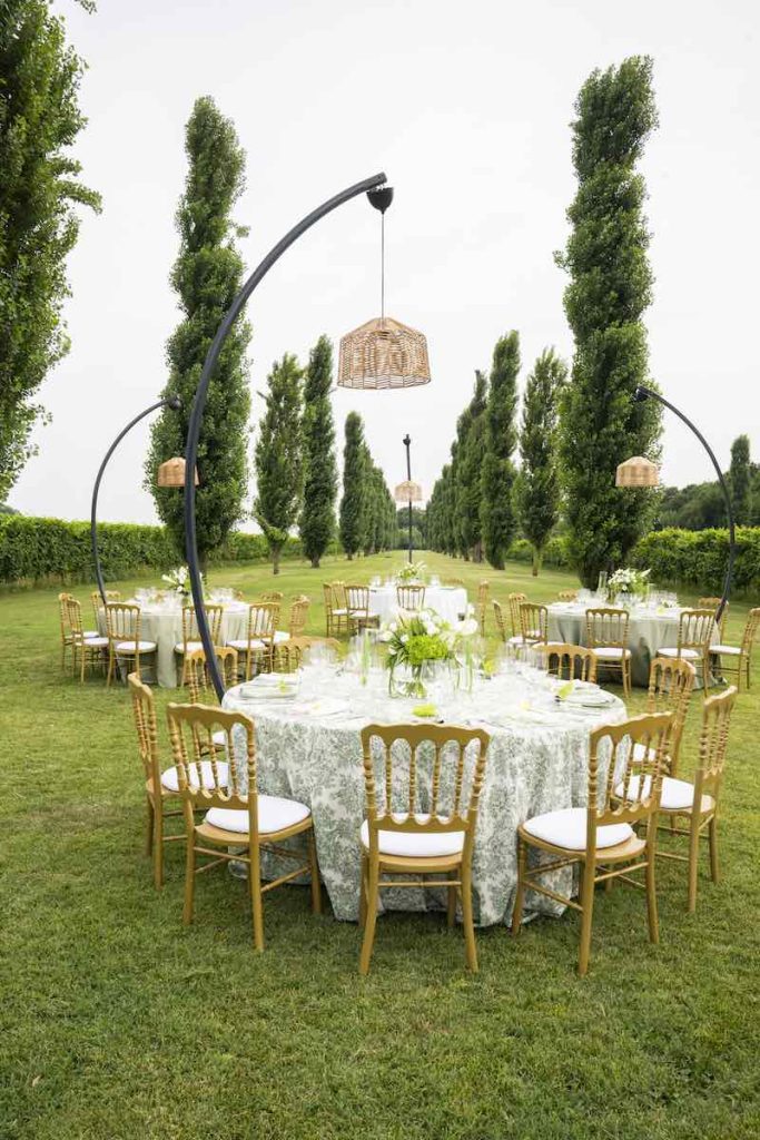 In questa foto un tavolo per un ricevimento di nozze di forma rotonda con tovagliato Toule de Jouy di colore verde sormontato da un lampadario in vimini