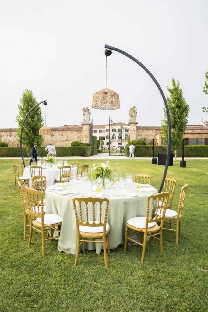 In questa foto un tavolo per un ricevimento di nozze di forma rotonda con tovagliato di colore verde sormontato da un lampadario in vimini