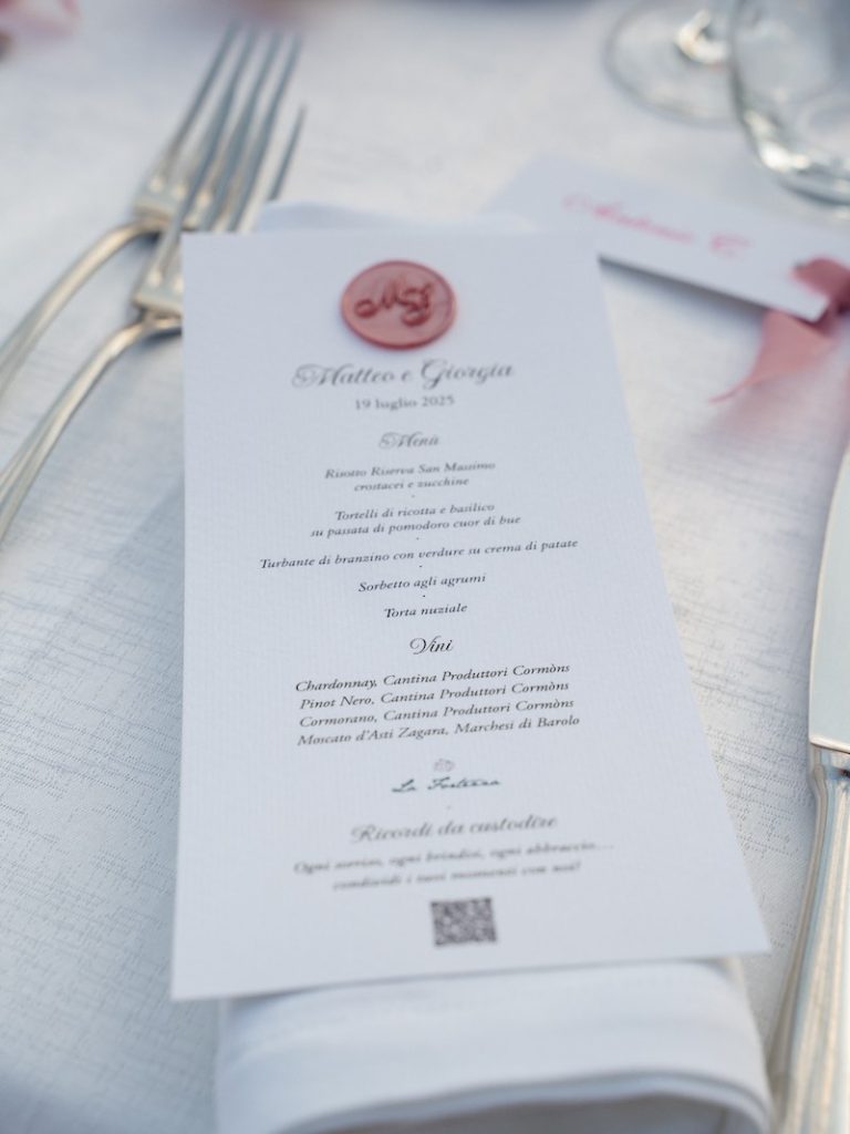 In questa foto, un menù per un matrimonio, di colore bianco con dettaglio di ceralacca con le iniziali degli sposi "M&G" di colore rosa
