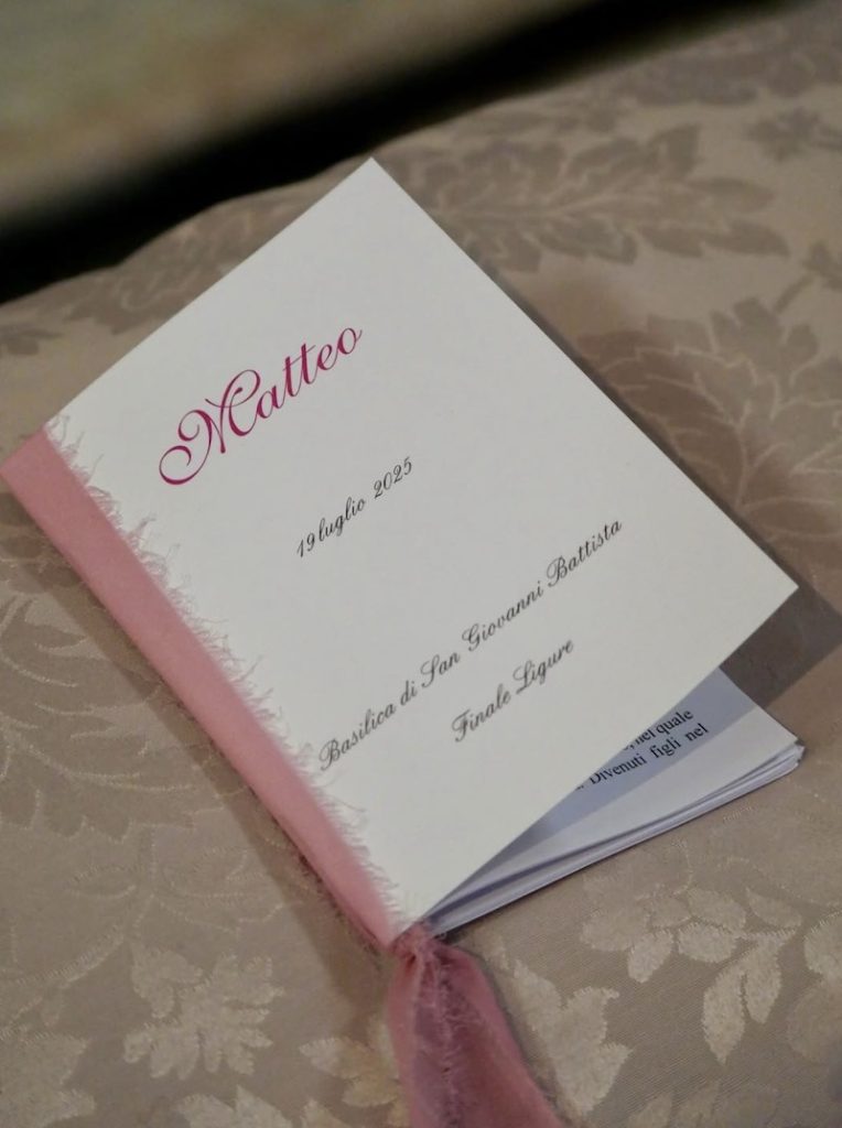 In questa foto, un libretto messa bianco con nastro di garza di colore rosa personalizzato con il nome dello sposo