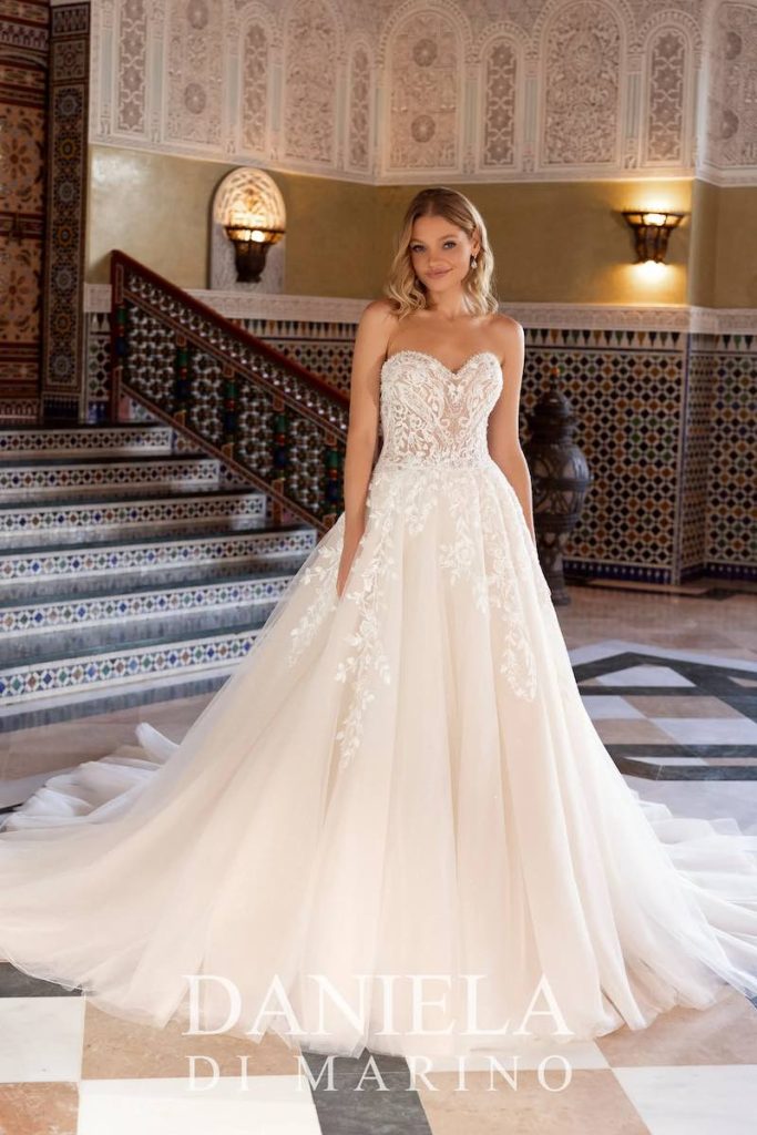 In questa foto, una modella posa indossando un abito da sposa Daniela Di Marino 2026 con silhouette ad A, gonna in tulle e corpetto con scollo a cuore e ramage floreale che scendono sulle lunghezze