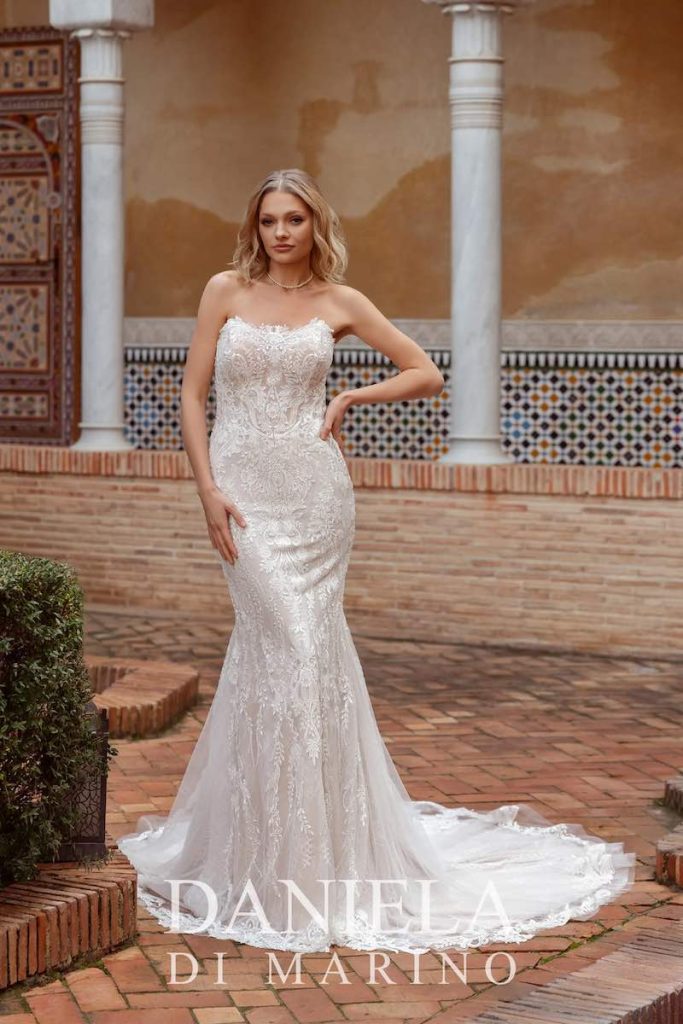 In questa foto, una modella posa indossando un abito da sposa Daniela Di Marino 2026 in pizzo, con ricami di perline, scollo dritto, silhouette a semisirena e lungo strascico