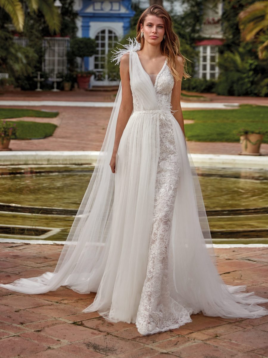 In questa foto si vede un abito da sposa in pizzo e tulle della collezione Manu Garcia che rappresenta una delle tendenze sposa 2026 . Il vestito ha un corpetto aderente con spalline , arricchito da una sovrapposizione di tulle drappeggiato su una spalla che crea un effetto fluido ed elegante. La silhouette è slanciata e femminile, con trasparenze sofisticate che esaltano la lavorazione del pizzo.