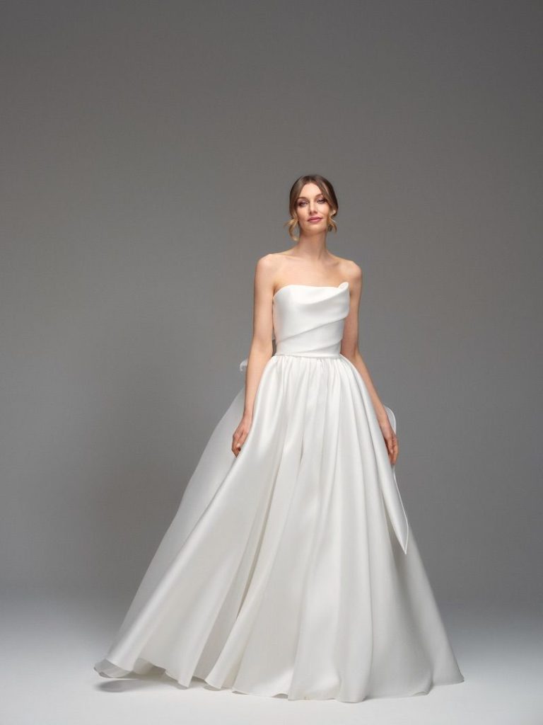 In questa foto si vede una modella che posa per un abito realizzato da Maria Pia Creazioni che rappresenta  al tendenza del drappeggio su del drappeggio su un abito minimal. Il bustier scultoreo esalta la figura donando un eleganza senza tempo 