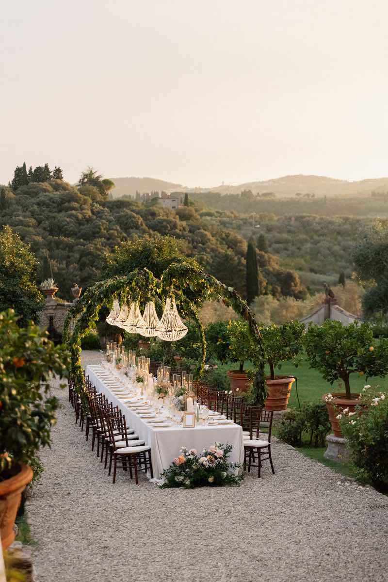 In questa foto uno dei matrimoni su misura firmati da The Couplers allestito in un giardino: un tavolo imperiale sormontato da lampadari chandelier e decorato con fiori e candele