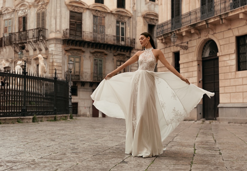 In questa foto, una modella posa a Palermo indossando un abito da sposa Monica Loretti 2026 con scollo all'americana, in chiffon e pizzo
