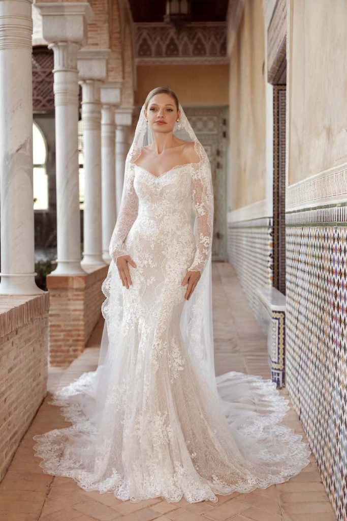 In questa foto, una modella posa indossando un abito a sirena in pizzo con velo abbinato della collezione Daniela Di Marino 2026