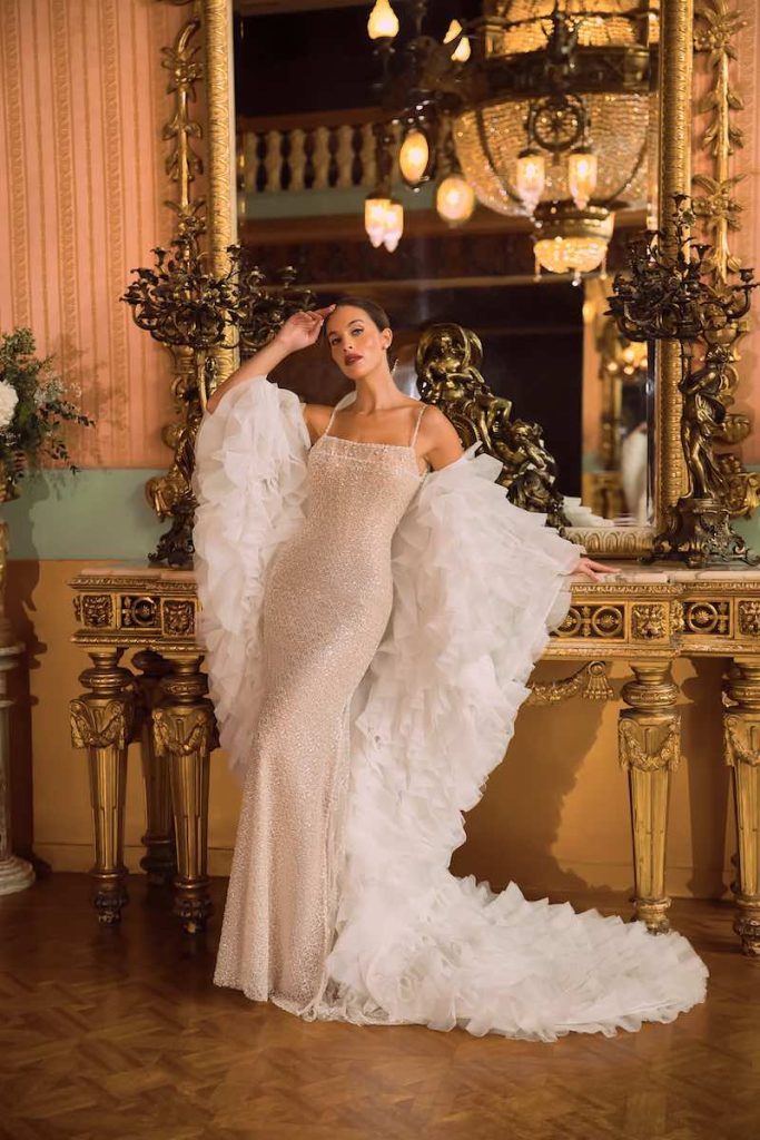 In questa foto, una modella posa indossando un abito da sposa con paillettes e perline abbinata ad una stola con ruches