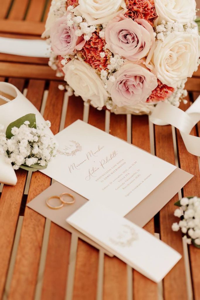In questa foto un dettaglio del bouquet della sposa con rose di colore rosa e bianco affiancato ad una partecipazione di nozze