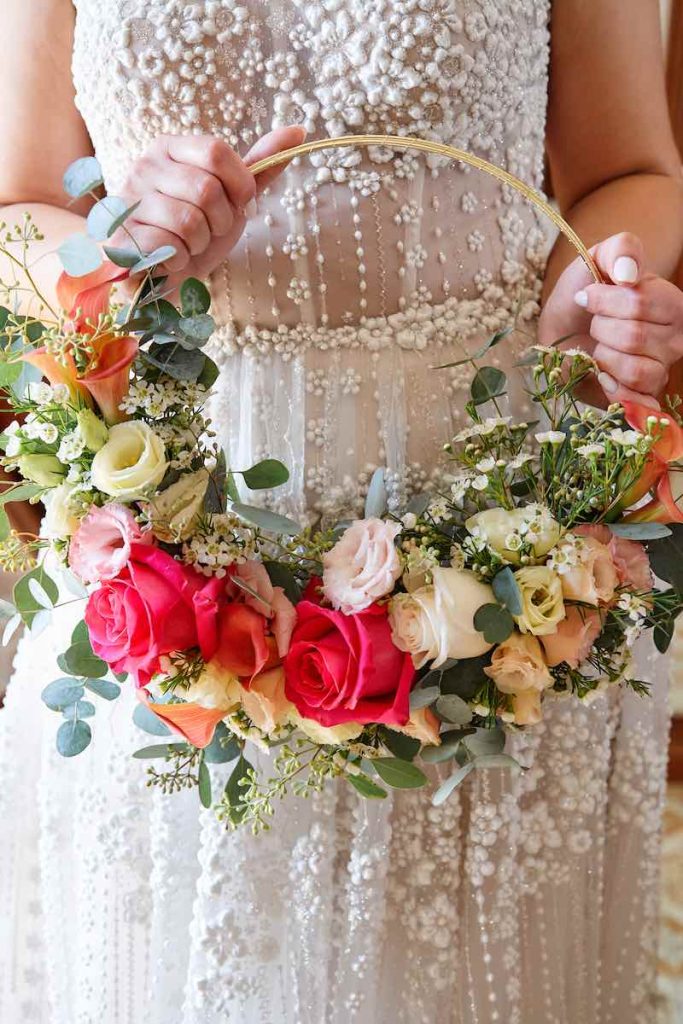 In questa foto un hoop bouquet con rose di colore fucsia e rosa, ranuncoli di colore bianco e foglie di salvia