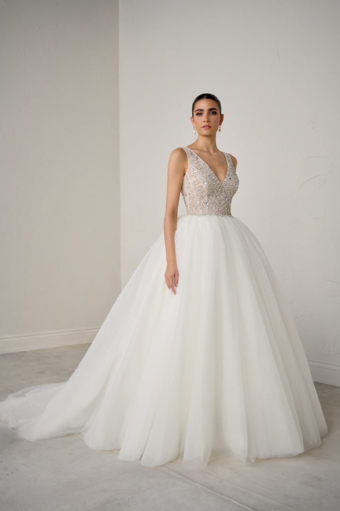 In questa foto, una modella posa  indossando un abito principessa con gonna in organza e corpetto ricamato con cristalli e perline della collezione sposa Justin Alexander Signature