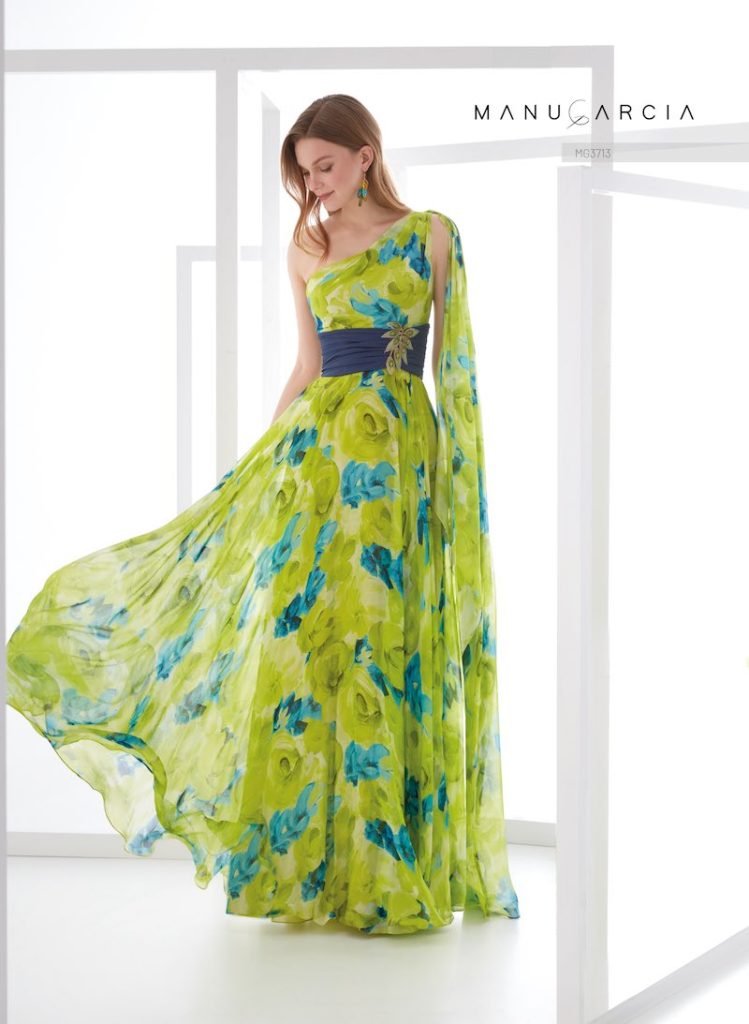 In questa foto, una modella posa indossando uno degli abiti da cerimonia Higar Novias Group 2026 della linea Manu García 2026 nei toni del verde e del blu cobalto con stampa floreale, scollo monospalla e cintura gioiello