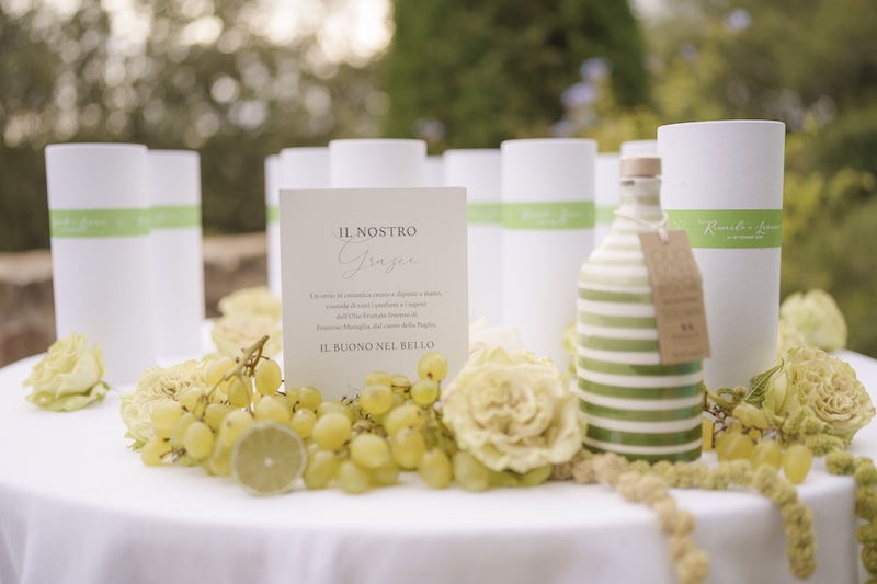 In questa foto un tavolo con bomboniere nei toni del verde e del bianco