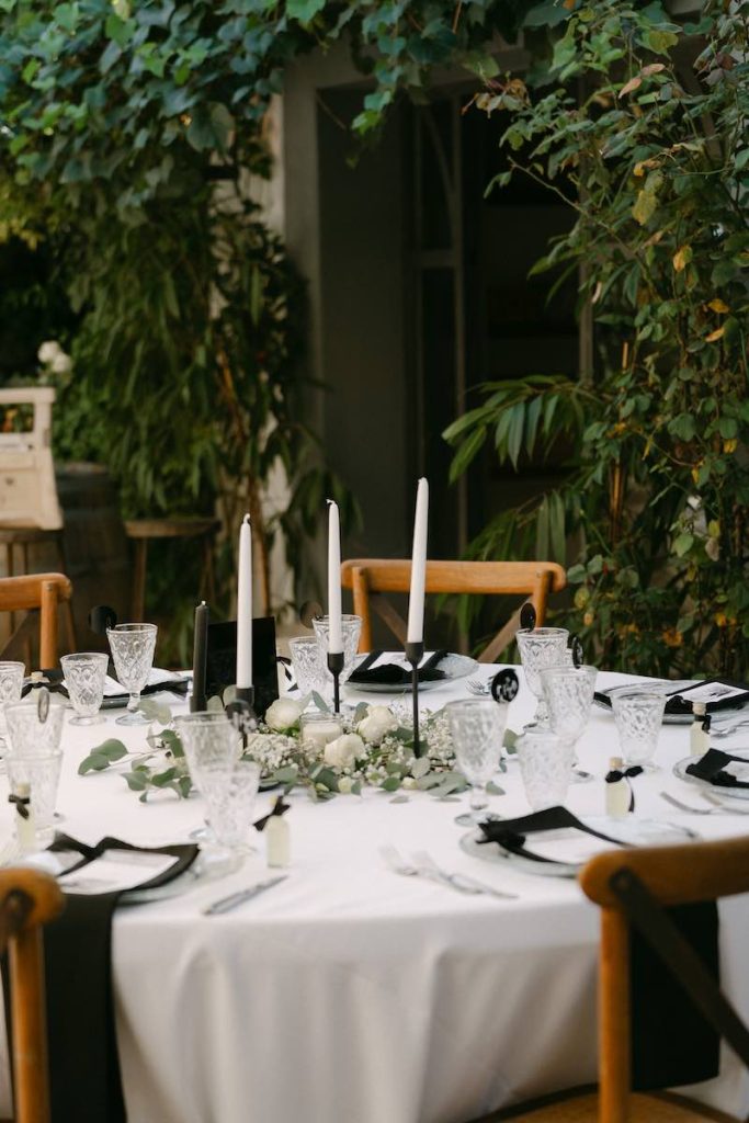 In questa foto, un tavolo rotondo allestito sotto ad un albero, nei toni bianco e nero