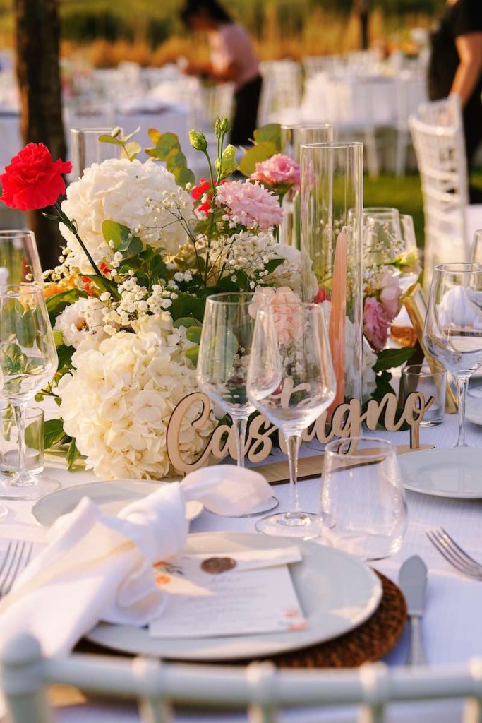 In questa foto il dettaglio di un tavolo per matrimonio decorato con i fiori e una targa di legno con il nome di un albero