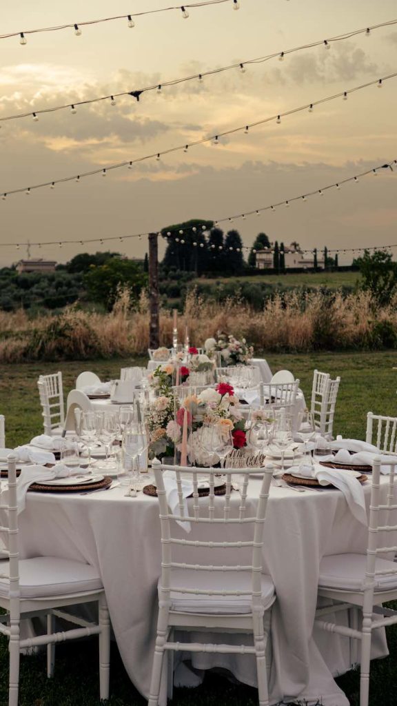 In questa foto l'allestimento di un matrimonio su un prato realizzato da Manuela Marrale con tavoli rotondi decorati con un centrotavola di fiori e chiavarine bianche