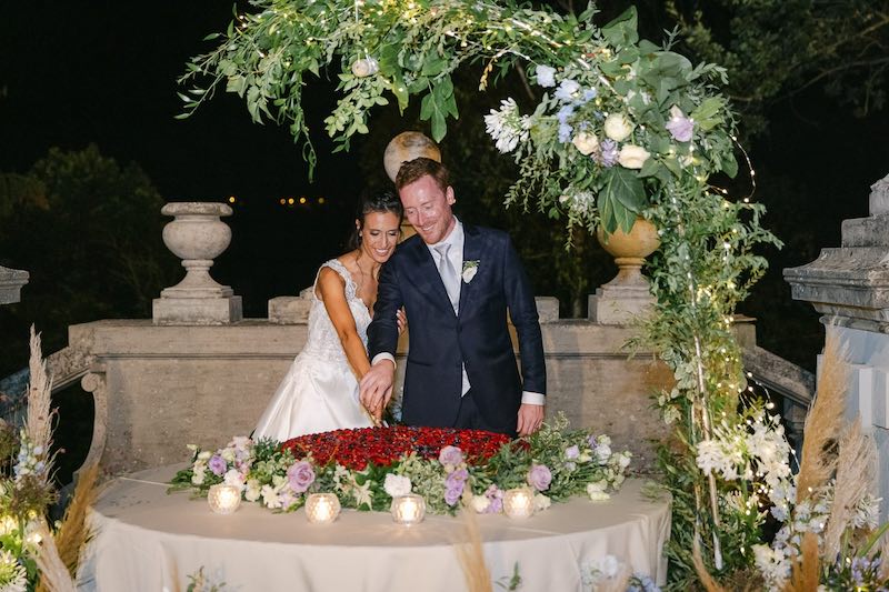 In questa foto due sposi tagliano una torta nuziale ad un piano con fragoline di bosco
