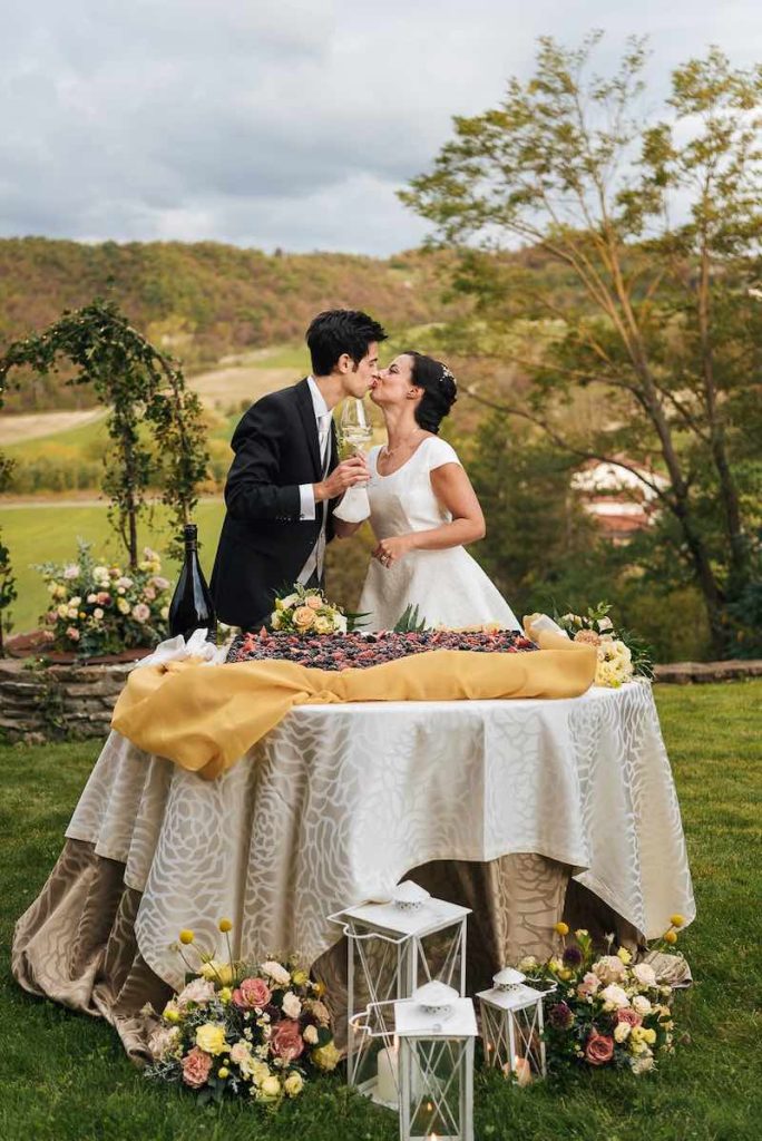 In questa foto due sposi brindano davanti ad una torta nuziale con frutti di bosco realizzata per un matrimonio firmato da Mariano Minetto