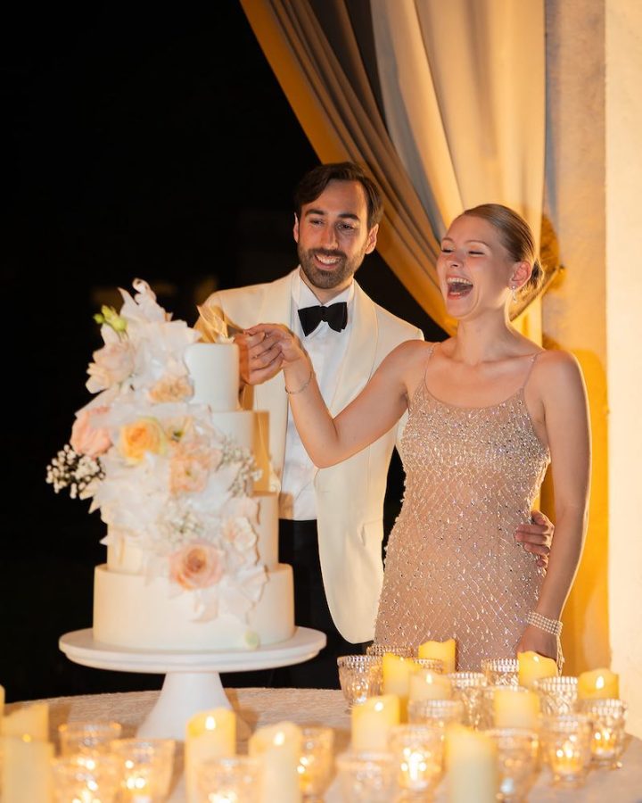 In questa foto, due sposi ridono al taglio della loro torta nuziale a piani decorata con fiori in nuance di rosa tra tante candele 