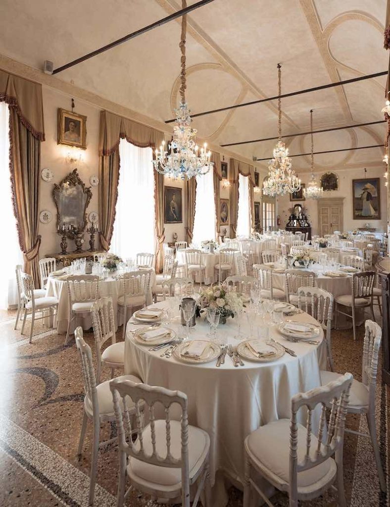 In questo foto la sala di un castello allestita per un matrimonio con tavoli rotondi e decorazioni floreali Total White