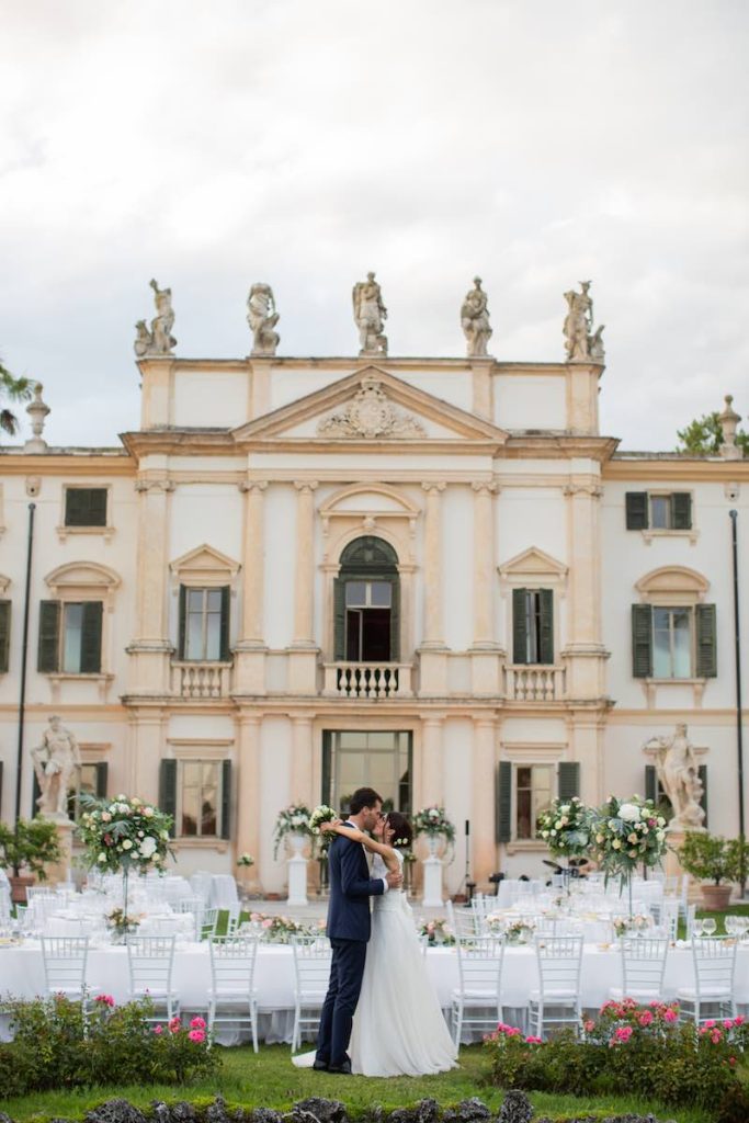 In questa foto, due sposi si baciano davanti all'allestimento del ricevimento in una villa storica