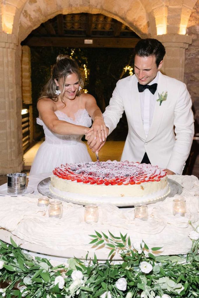 In questa foto, due sposi mentre tagliano una torta ad un piano con frutti di bosco