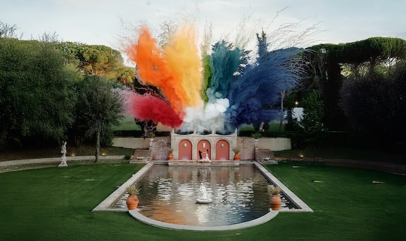 In questa foto due sposi posano davanti ad una fontana rettangolare illuminata da fuochi d'artificio colorati