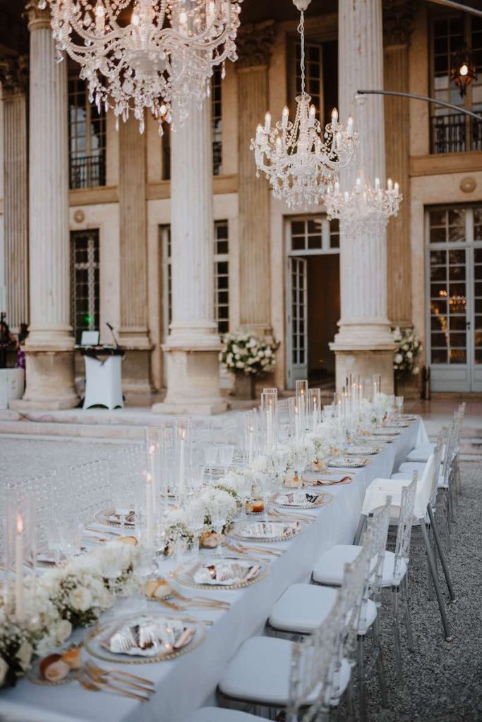 In questa foto un tavolo imperiale allestito con fiori di colore bianco e stoviglie di colore oro e argento per un matrimonio davanti alla facciata di un dimora storica 