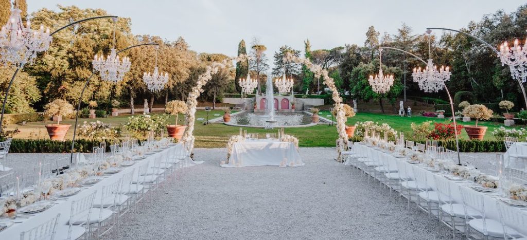 In questa foto un allestimento firmato da Tatiana Tabanelli per un ricevimento di nozze realizzato con due tavoli imperiali e un arco floreale con lampadari chandelier al centro del quale è posizionato il tavolo degli sposi