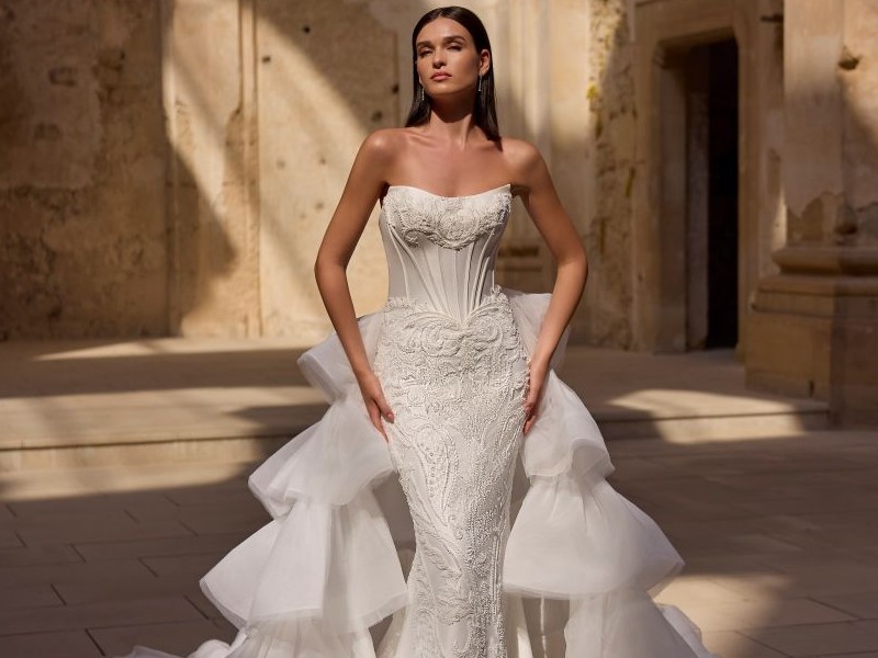 In questa foto, una modella indossa un abito da sposa particolarmente scenografico con bustier a cuore, ricami elaborati e una gonna in tulle vaporoso a strati che si apre sul retro come una cascata. Il look fa parte della collezione di abiti da sposa particolari 2026.