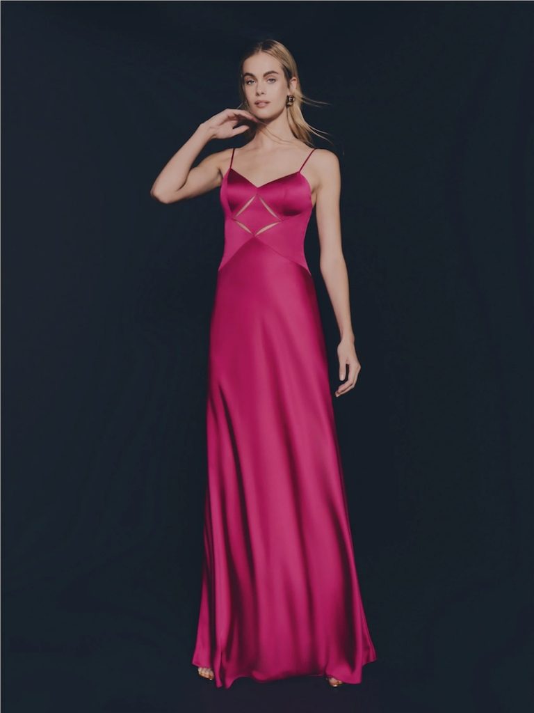 In questa foto una modella posa indossando un abito da cerimonia Pronovias 2026 di colore fucsia, modello scivolato, con dettaglio cut-out sul busto