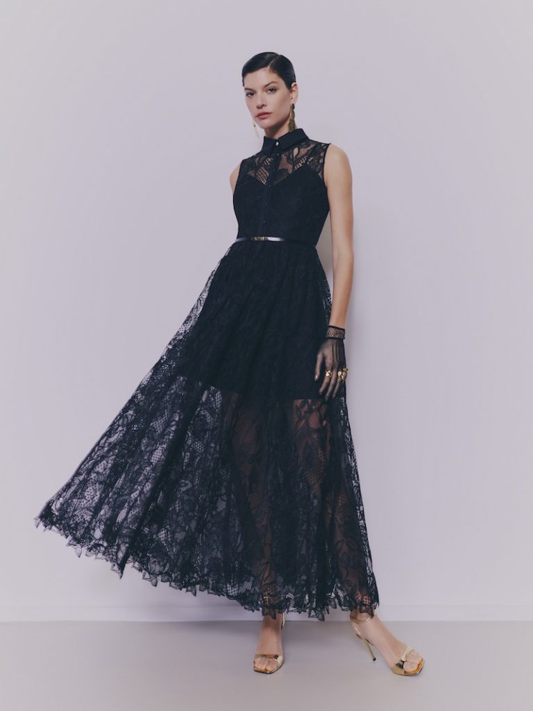 In questa foto una modella posa indossando uno degli abiti da cerimonia Pronovias 2026 di colore blu notte in pizzo, modello midi con gonna a campana e colletto