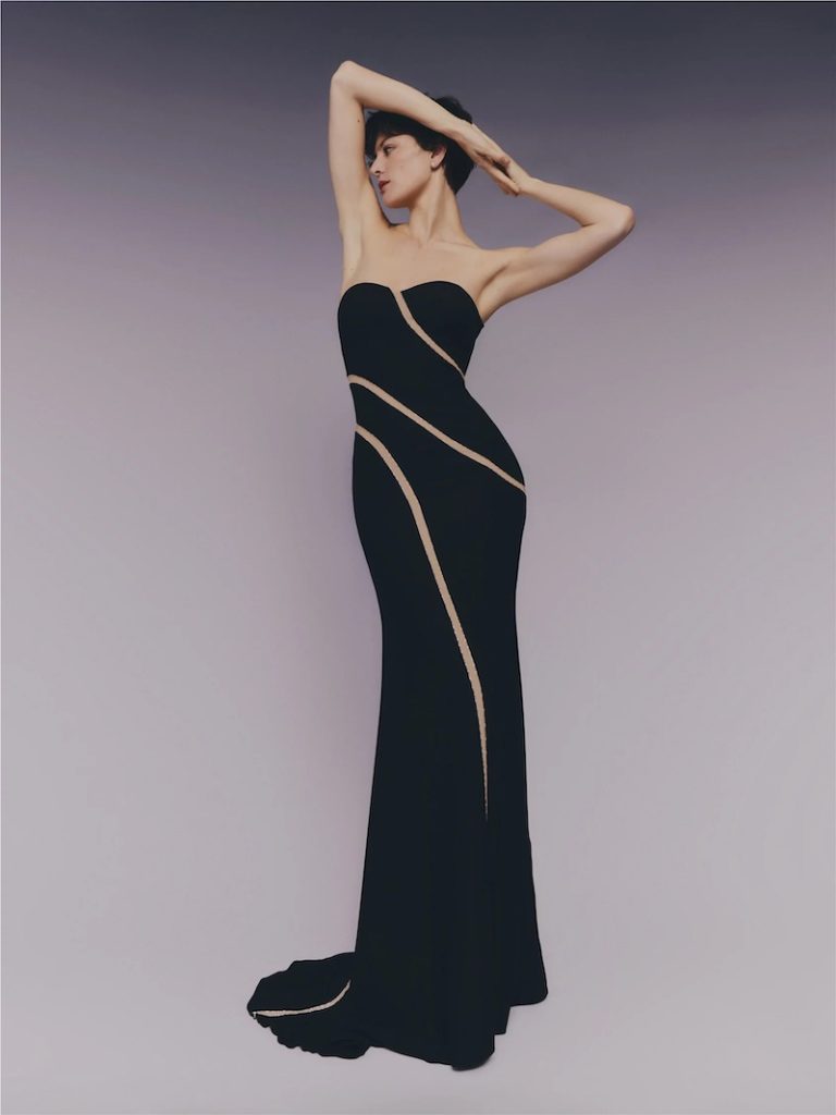 In questa foto una modella posa indossando un abito da cerimonia Pronovias 2026 di colore nero, modello a sirena, scollo a cuore e linee sinuose trasparenti sulla lunghezza