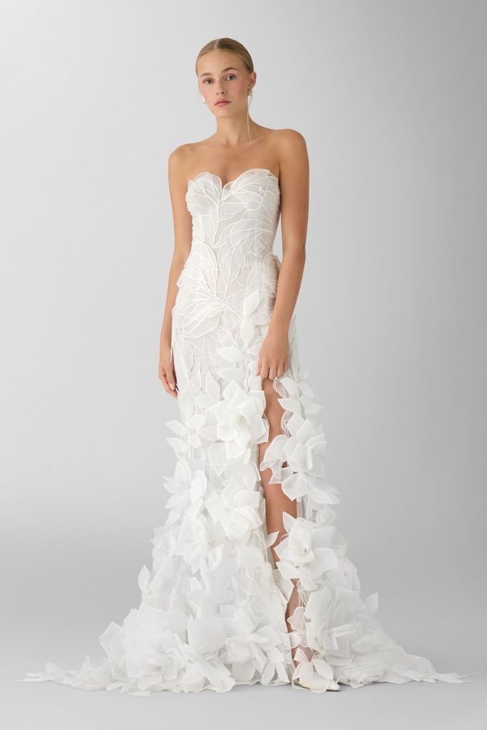 In questa foto, la sposa sfoggia un abito aderente con decorazioni a foglia e fiori tridimensionali applicati lungo la gonna, che si apre con uno spacco sensuale. L’outfit è un esempio perfetto di abiti da sposa particolari 2026 dallo stile audace e creativo.