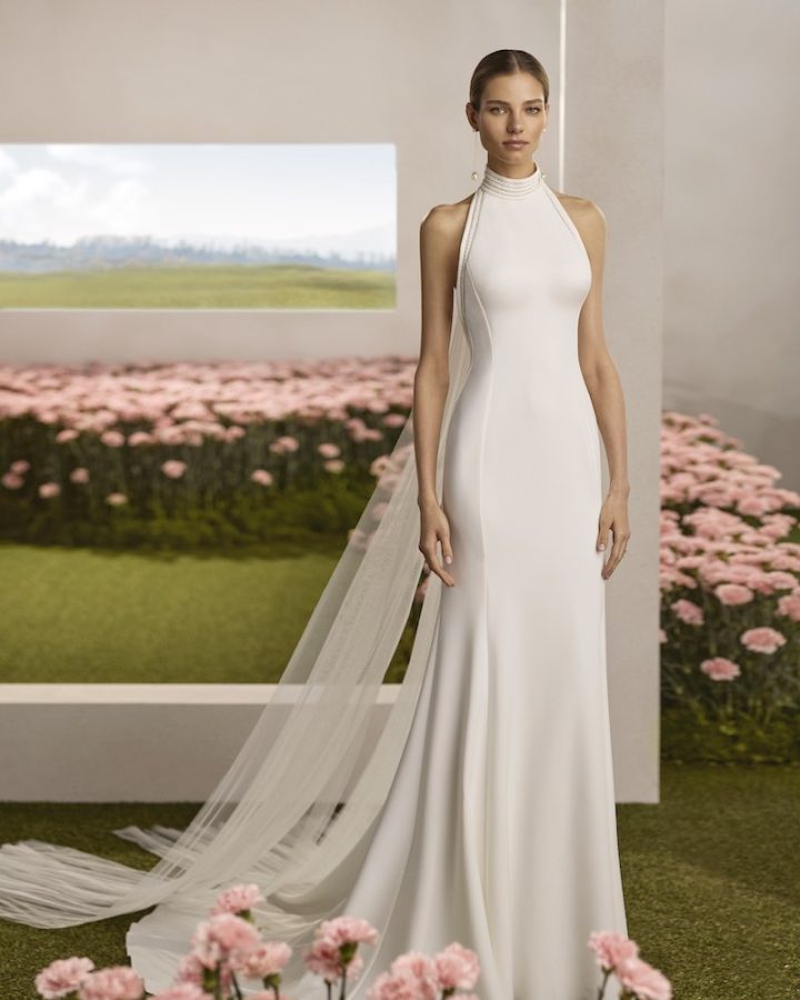 In questa foto, una modella posa indossando un abito da sposa Rosa Clará Couture 2026 a semi-sirena con scollo all'americana con dettagli di perle