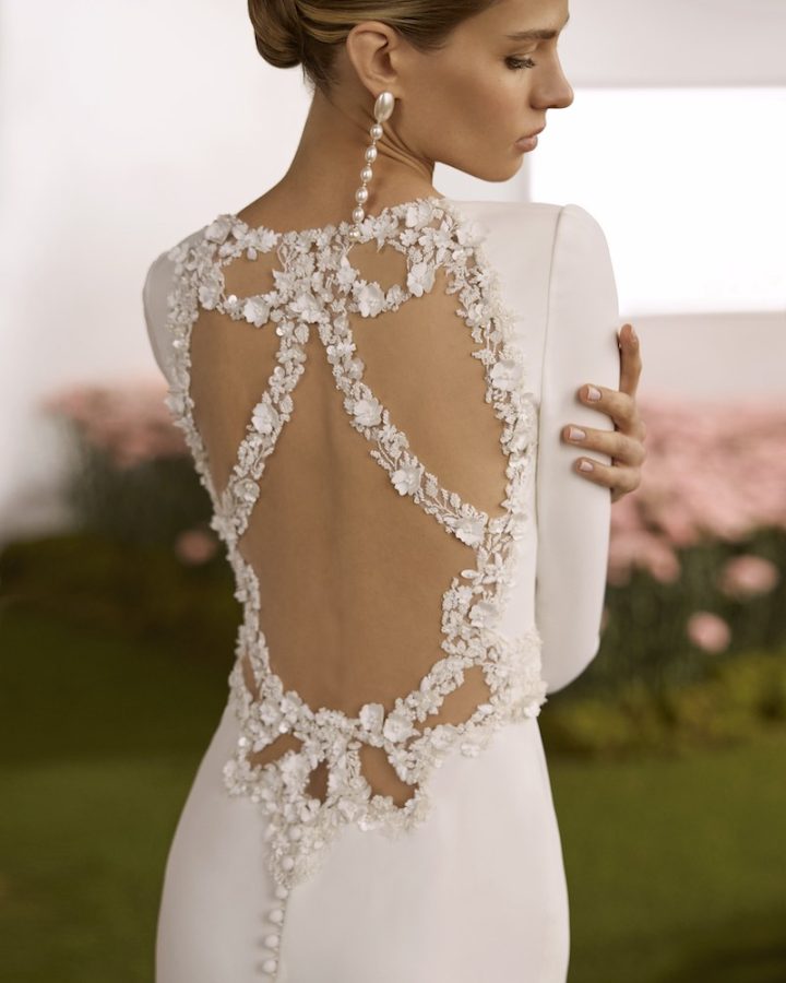 In questa foto, una modella posa di spalle indossando un abito da sposa mostrando una schiena riccamente decorata con fiori 3D gioiello