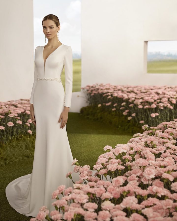 In questa foto, una modella posa indossando un abito da sposa Rosa Clará Couture 2026 a semi sirena con maniche lunghe e scollo a V