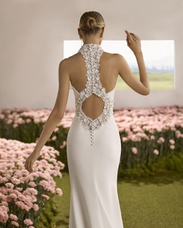 In questa foto, una modella posa di spalle indossando un abito da sposa mostrando una schiena riccamente decorata con fiori 3D gioiello
