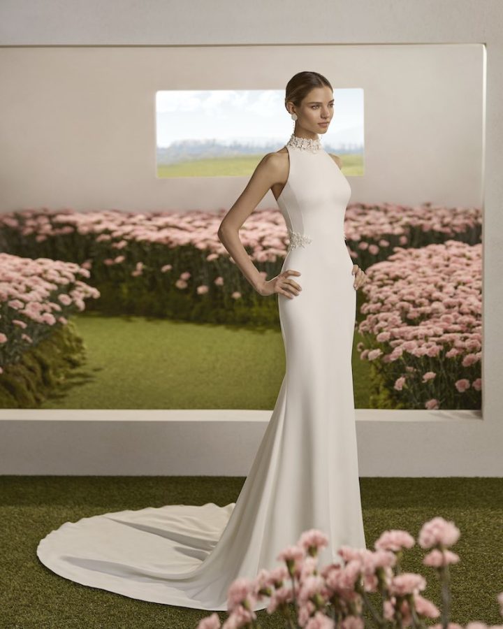 In questa foto, una modella posa indossando un abito della collezione sposa Rosa Clará Couture 2026 a sirena, in crêpe, con scollo all'americana e applicazioni gioiello