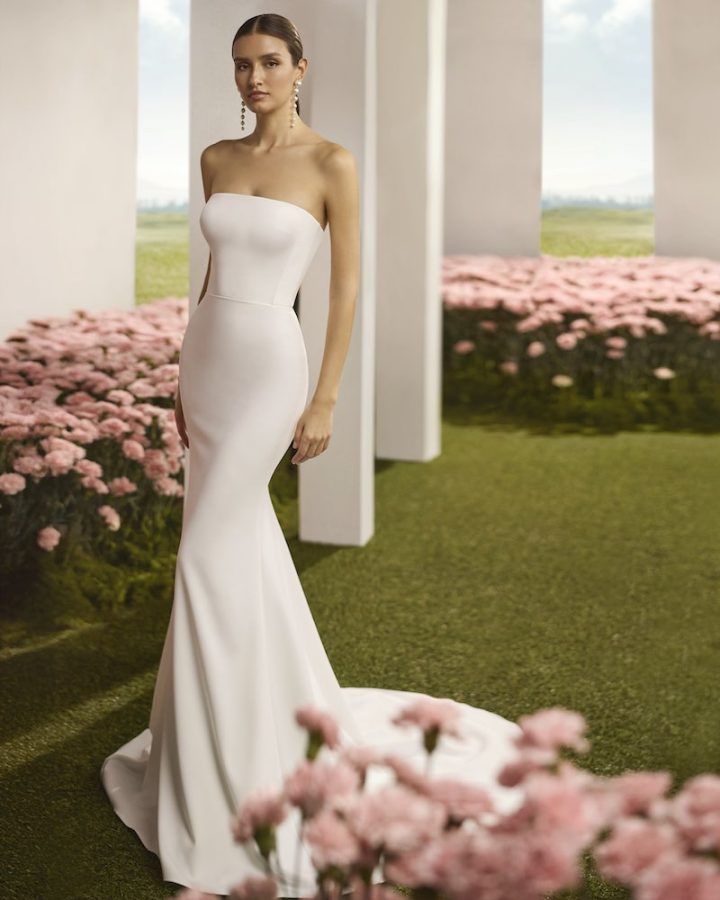In questa foto, una modella posa indossando un abito della collezione sposa Rosa Clará Couture 2026 a sirena con corpetto senza maniche e dritto