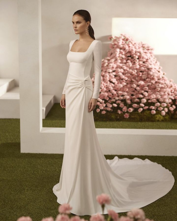 In questa foto, una modella posa indossando un abito della collezione sposa Rosa Clará Couture 2026 a sirena in cady, con drappeggio laterale, maniche e scollo quadrato