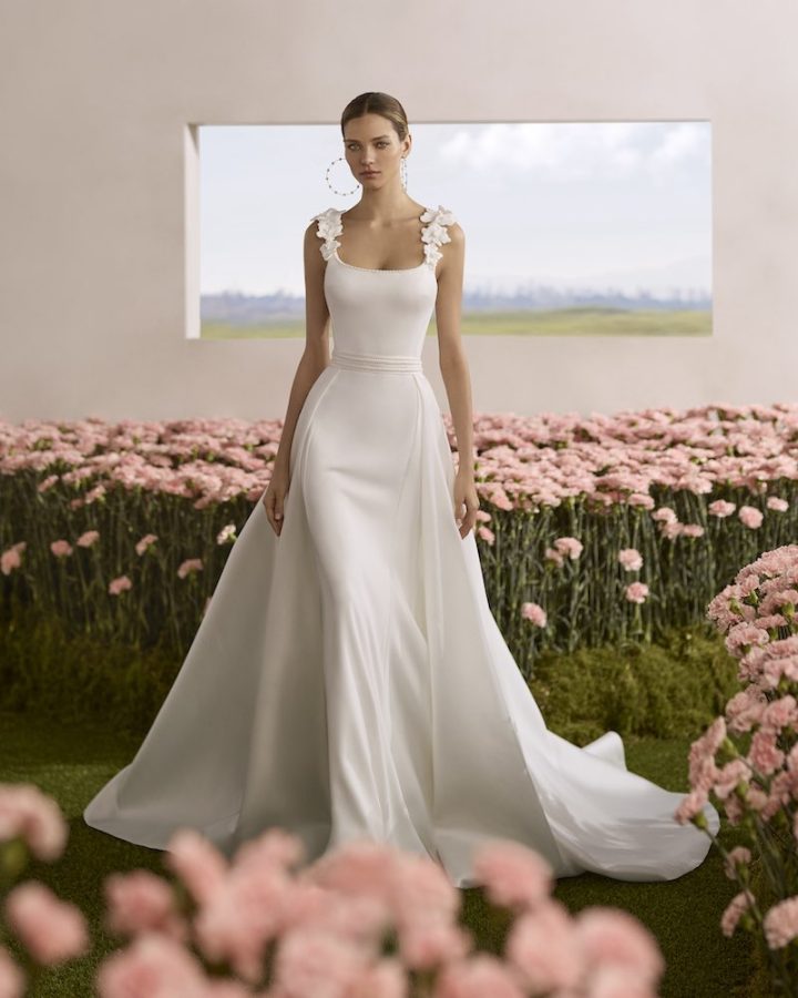 In questa foto, una modella posa indossando un abito da sposa a sirena in cady, con sopragonna removibile e fiori 3D sulle bretelle