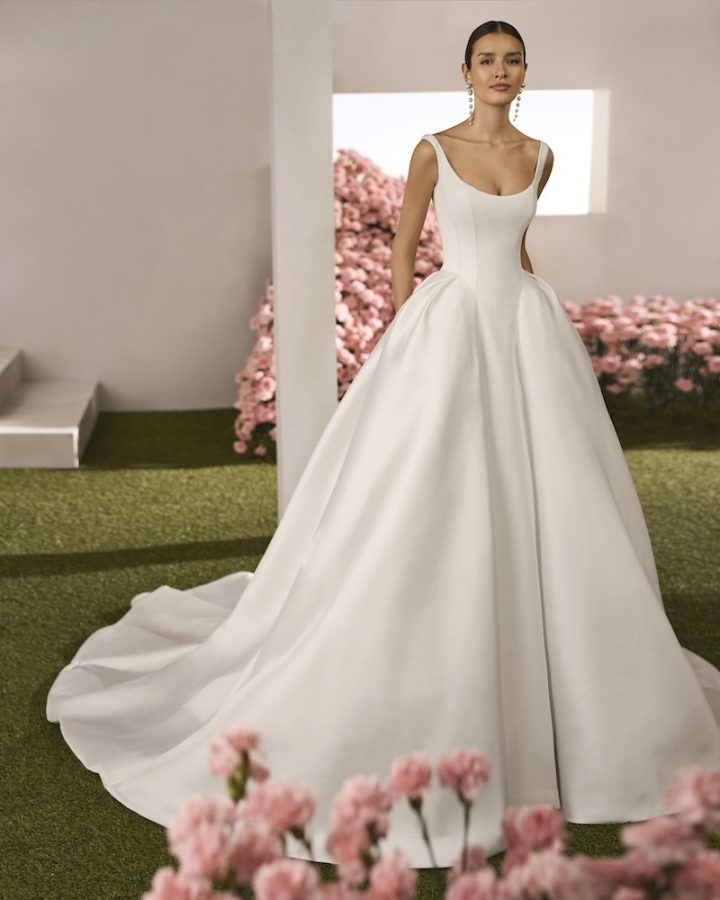 In questa foto, una modella posa indossando un abito della collezione sposa Rosa Clará Couture 2026 in mikado, modello principessa con corpetto a vita basca e scollo rotondo