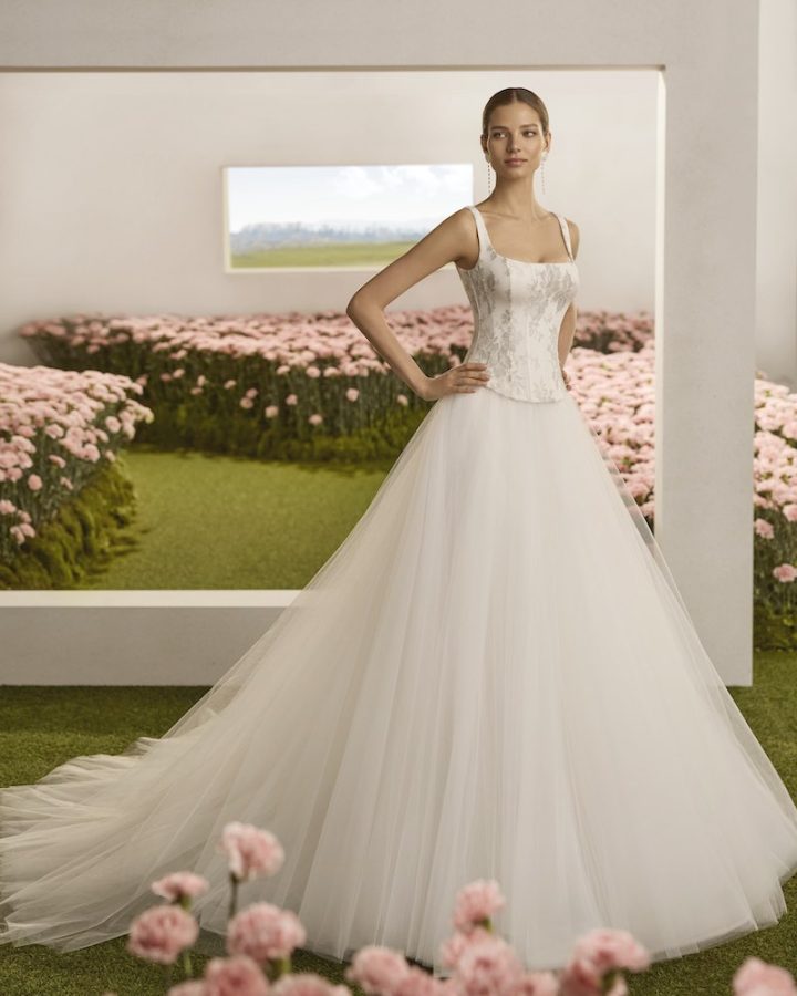 In questa foto, una modella posa indossando un abito della collezione sposa Rosa Clará Couture 2026 con taglio principessa, corpetto a vita basca ricamato con fili argento e gonna in tulle