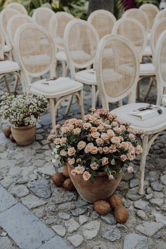 In questa foto l'allestimento di una cerimonia di nozze all'aperto con fiori dai colori tenui e rose e sedie vintage