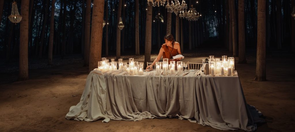 In questa foto, la Wedding Planner Giulia Ferro di Maritari mentre allestisce una tavola di nozze nel bosco, con una tovaglia verde salvia e candele