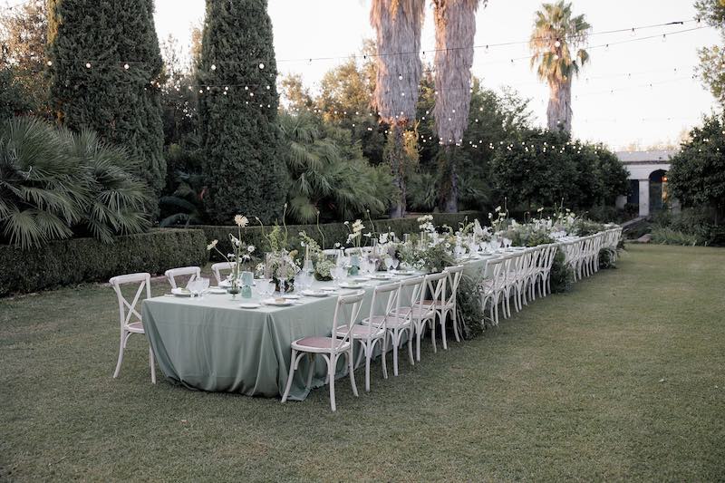 In questa foto un grande tavolo imperiale allestito nei toni del verde e del bianco in un giardino