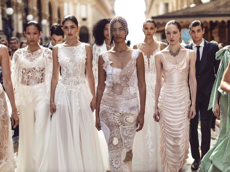 In questa foto alcune modelle in abiti da sposa sfilano nella galleria del Duomo di Milano per il Sì Sposaitalia Collezioni 2026